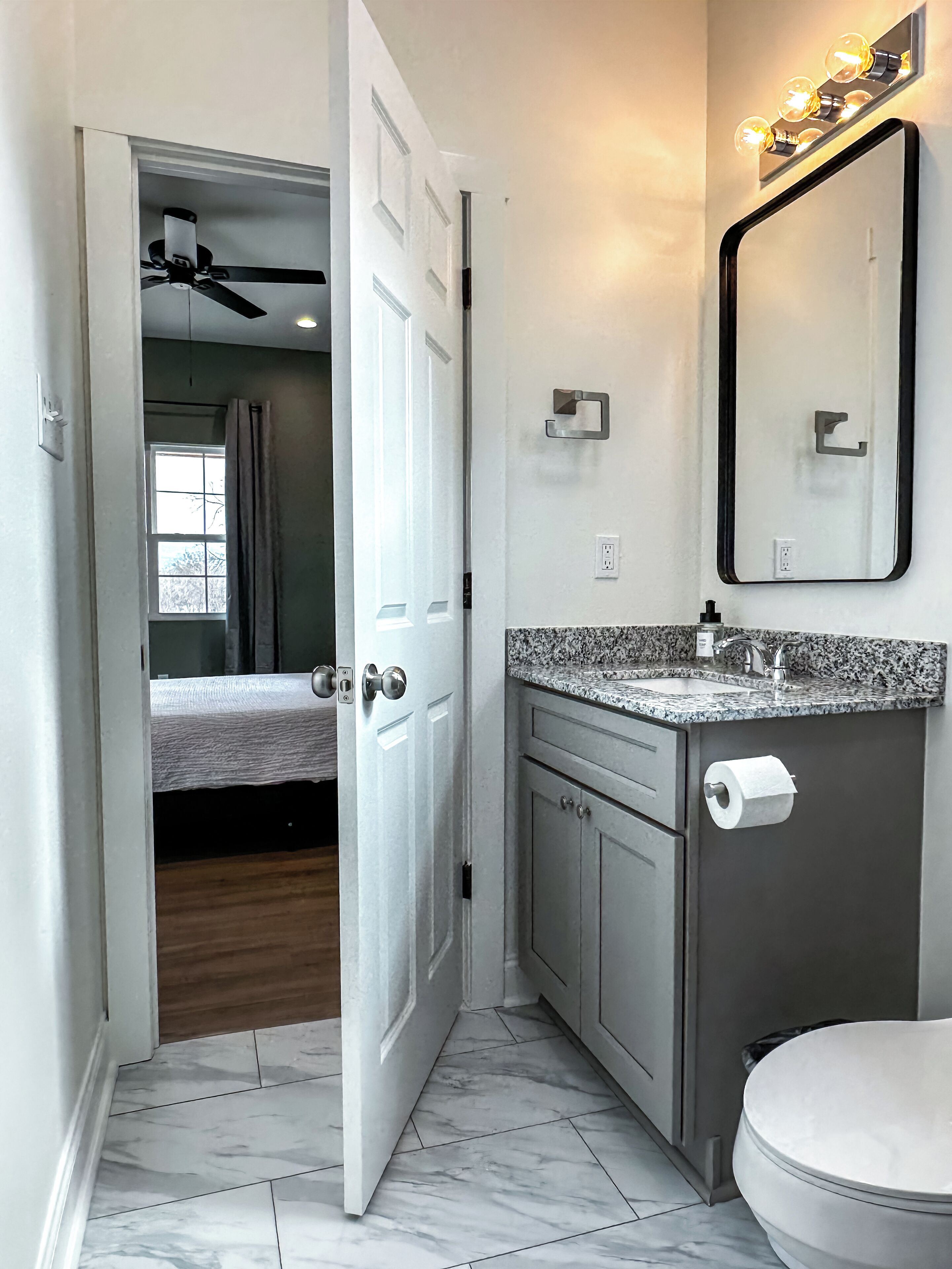 A modern bathroom with a marble floor, a sink with a faucet, a toilet, and a mirror with lights.