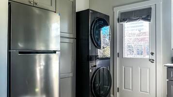 Una cucina con un frigorifero in acciaio inossidabile, una lavatrice nera e una porta bianca con finestra.
