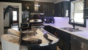 A modern kitchen with black cabinets, a stainless steel stove, a microwave, and a large island with a sink. - Beautiful 3 bedroom uniquely designed home for small to large families! Pets ok! (Davenport)