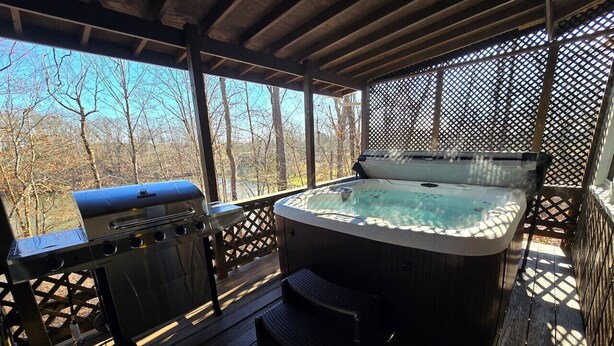 Una terraza techada al aire libre con un jacuzzi, una parrilla y una mesa de madera.
