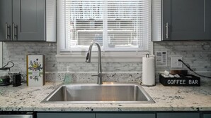 Una cocina con un lavamanos de acero inoxidable, una ventana con persianas, un letrero que dice ‘cafetería’ y un dispensador de pañuelos.