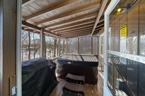 A covered outdoor area with a hot tub, wooden deck, and a view of a snowy landscape.