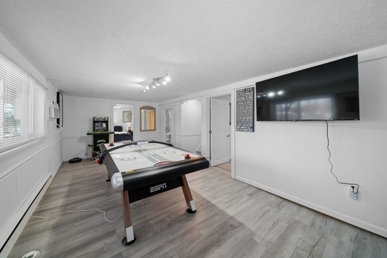 A room with a pool table, a flat-screen TV mounted on the wall, and a window with blinds.