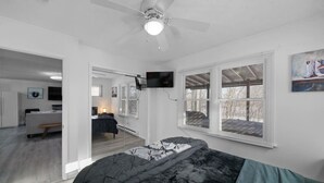 Un dormitorio con cama, ventilador de techo, televisión montada en la pared y ventana con persianas.