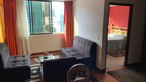 Ein modernes Wohnzimmer mit Sofa, Sessel und Couchtisch. Ein großes Fenster bietet Blick auf Gebäude.