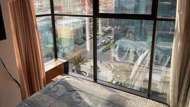 Ein Zimmer mit großem Fenster und Blick auf eine Stadtlandschaft, mit modernen Gebäuden und einer belebten Straße.