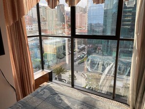 A room with a large window overlooking a cityscape, featuring modern buildings and a busy street.
