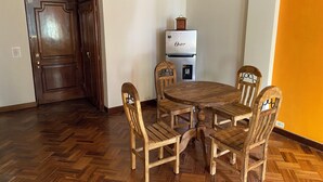Ein Essbereich mit einem Holztisch, Stühlen, einem Kühlschrank und einer Uhr darauf.