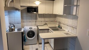Eine kompakte Küche mit Mikrowelle, Waschmaschine, Spüle und einem kleinen Tisch.