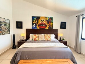 Ein Schlafzimmer mit einem großen Bett, zwei Nachttischen mit Lampen, einem hölzernen Kopfteil und einem Gemälde über dem Bett.