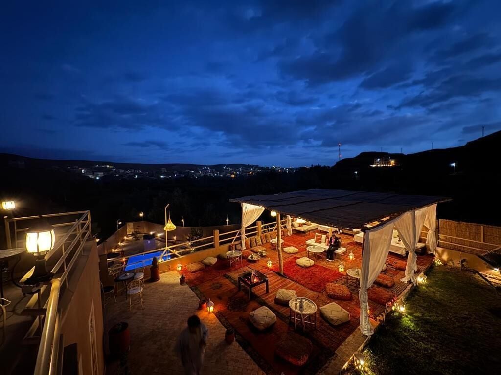 A rooftop terrace with outdoor seating, a pool, and a view of the city at night.