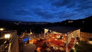A rooftop terrace with outdoor seating, a pool, and a view of the city at night.