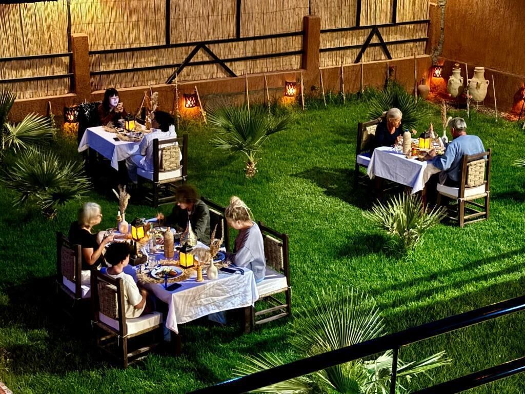 An outdoor dining area with tables and chairs, surrounded by greenery and decorative lanterns.