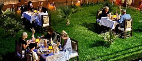 An outdoor dining area with tables and chairs, surrounded by greenery and decorative lanterns.