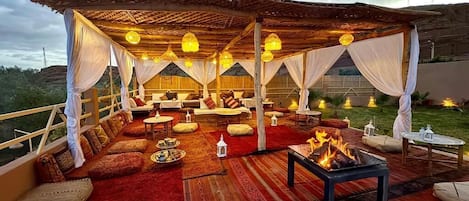 An outdoor seating area with a fire pit, cushioned seating, and hanging lanterns.