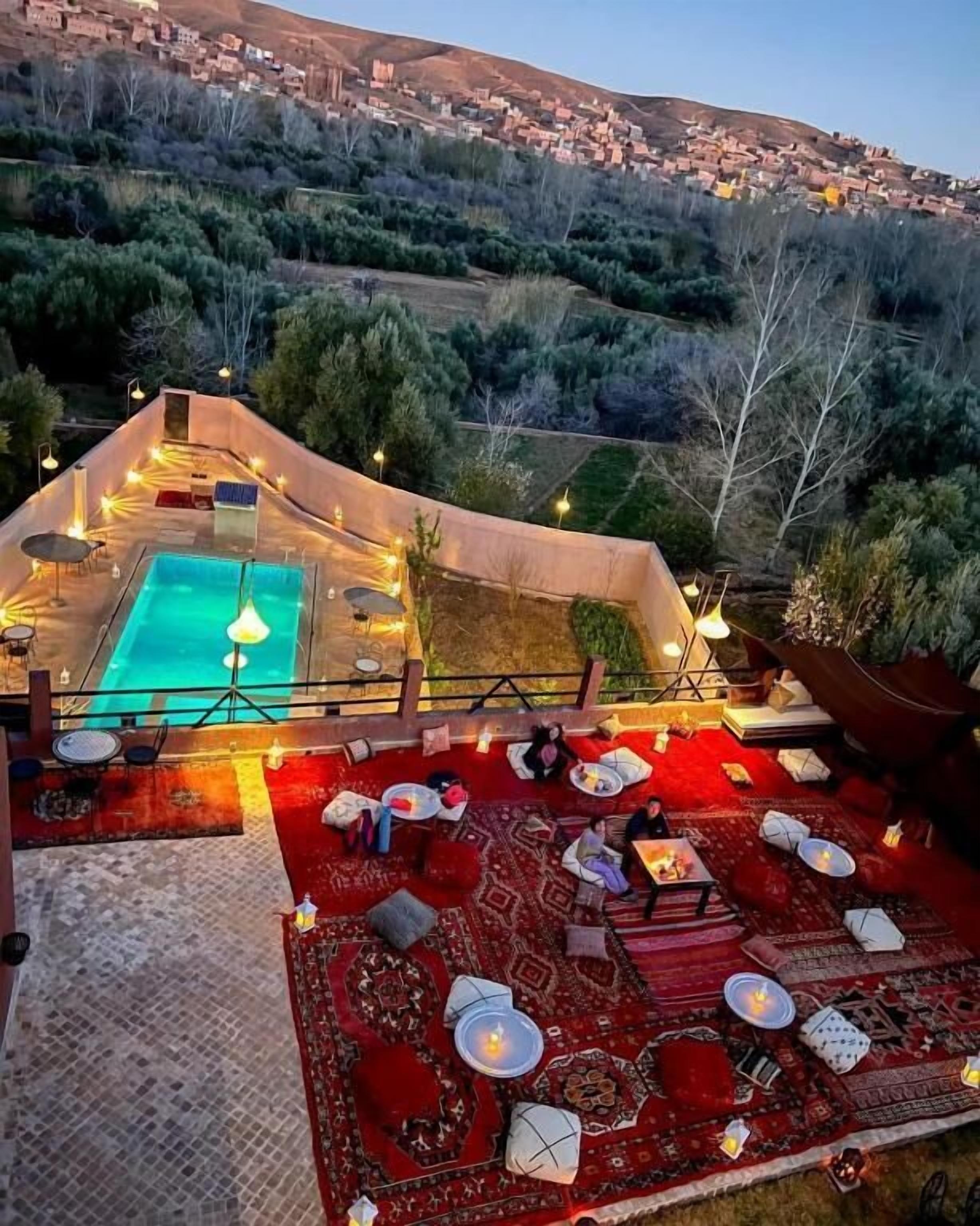 An outdoor pool area with a red carpet and seating, surrounded by a hillside view.