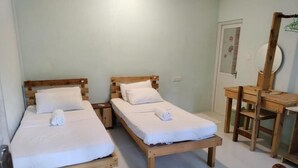 Two wooden beds with white linens and towels, a wooden desk, and a mirror in a room with light-colored walls and tiled flooring. - Evot Wave (Himmafushi)