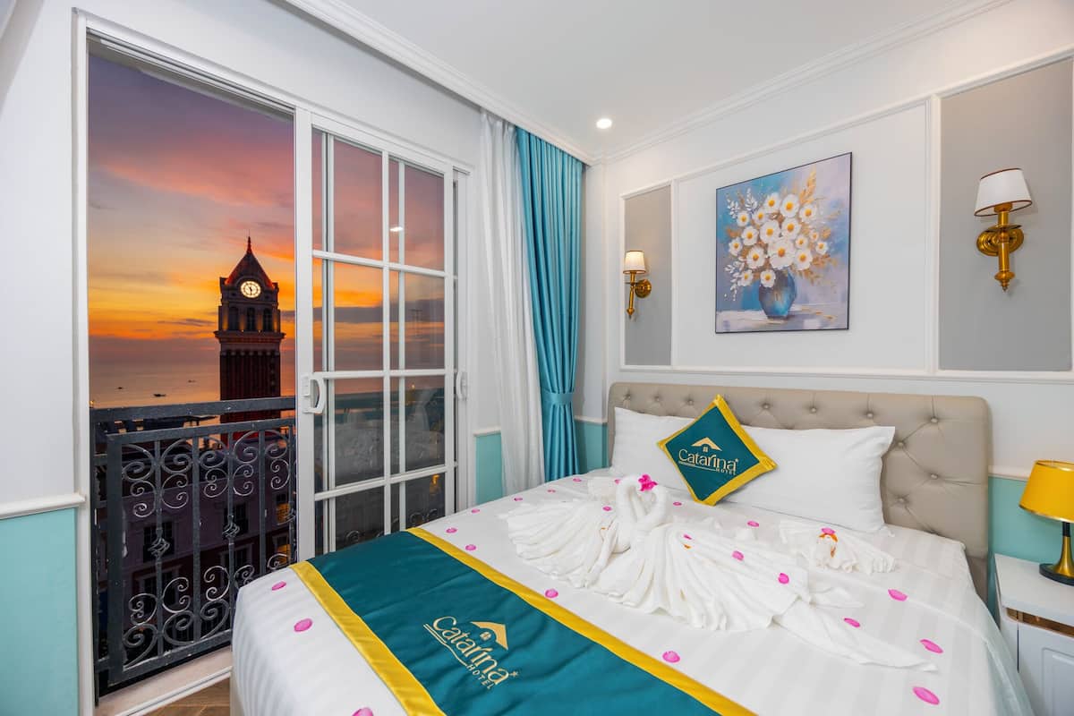 A hotel room with a bed, a painting, a lamp, and a view of a clock tower.