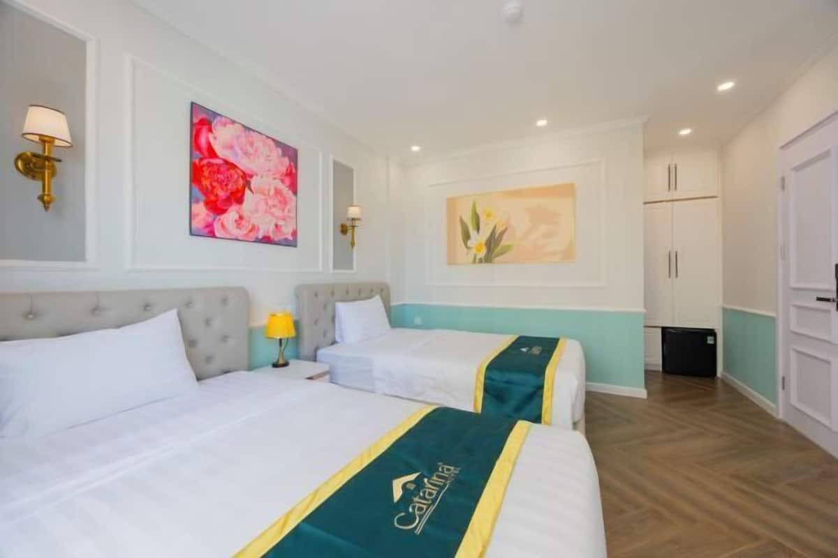 A hotel room with two beds, a nightstand, a lamp, and artwork on the walls.