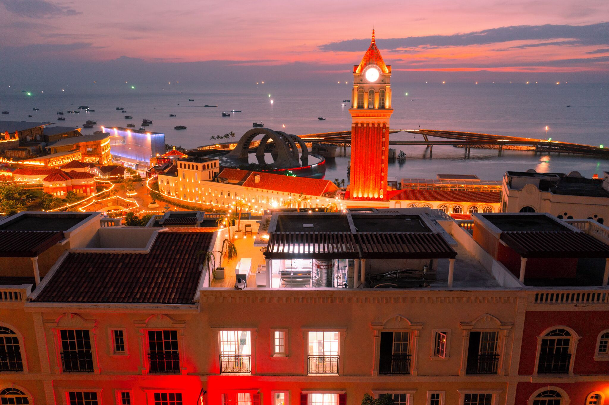 A coastal cityscape with a prominent clock tower, a bridge, and a waterfront promenade.
