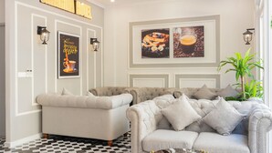 Een hotel lobby met een zwart-wit schakeerd motief op de vloer, twee banken, ingelijste kunstwerken en een plafondventilator.