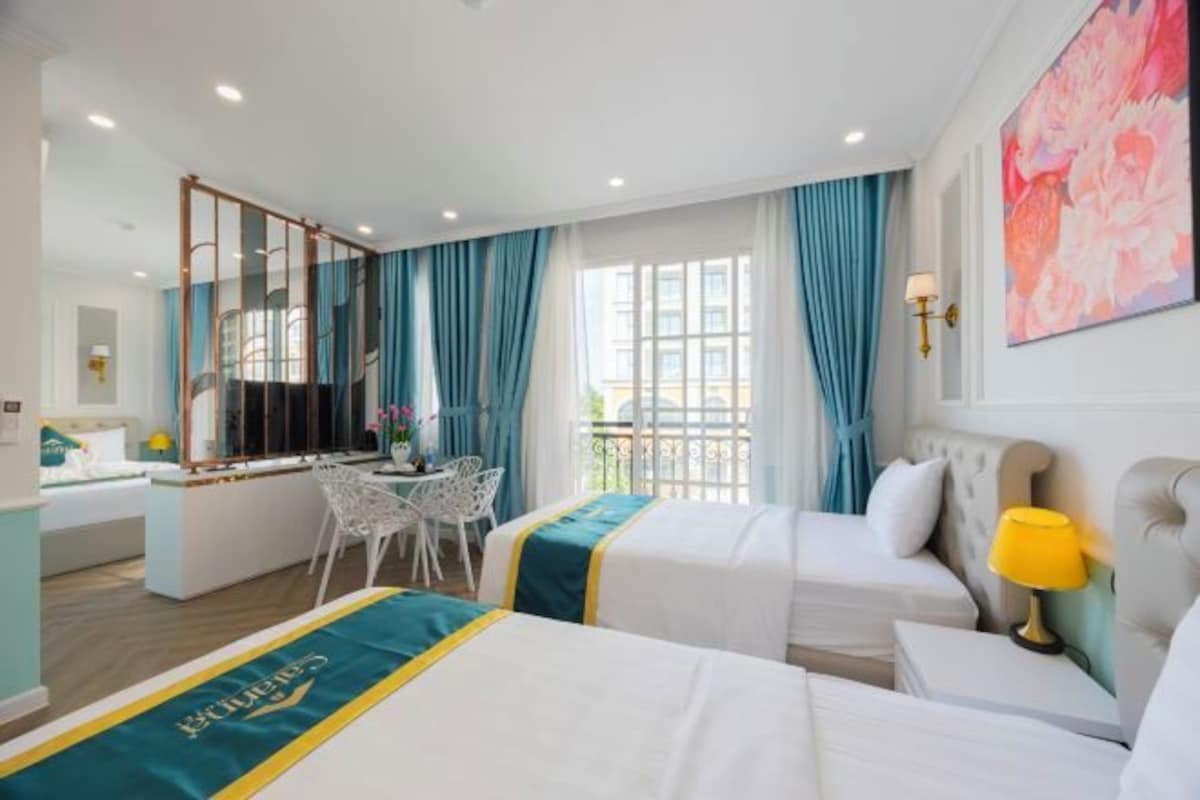 A hotel room with two beds, a desk, a chair, and a balcony with curtains.
