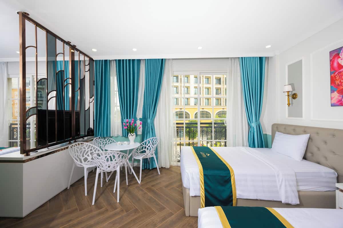 A hotel room with a bed, a dining table with chairs, a window with curtains, and a view of buildings outside.