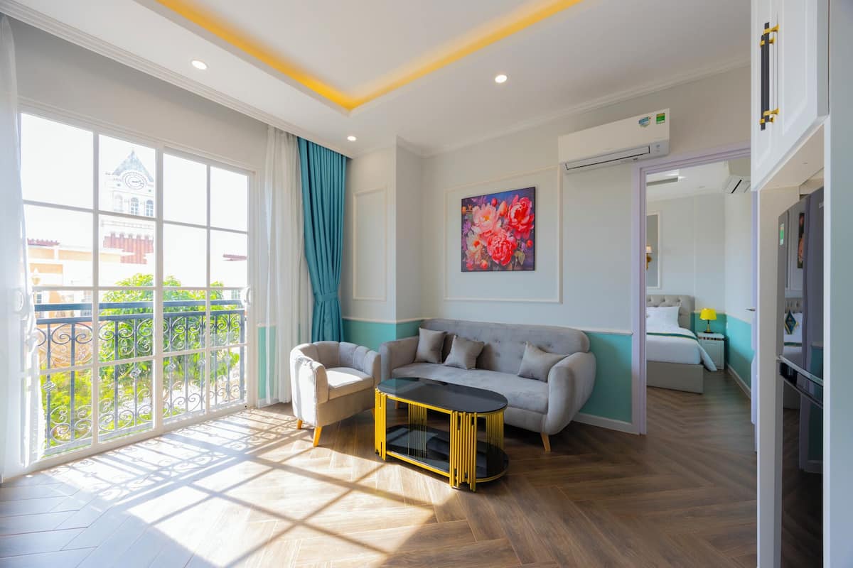 A modern living room with a sofa, armchair, and coffee table. There is a large window with a view of greenery and a building.