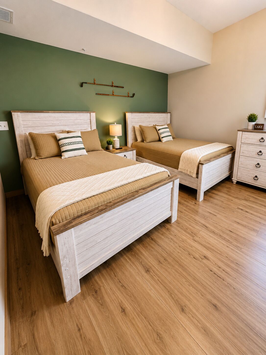 A bedroom with two beds, a nightstand with a lamp, a dresser, and a wall-mounted shelf.