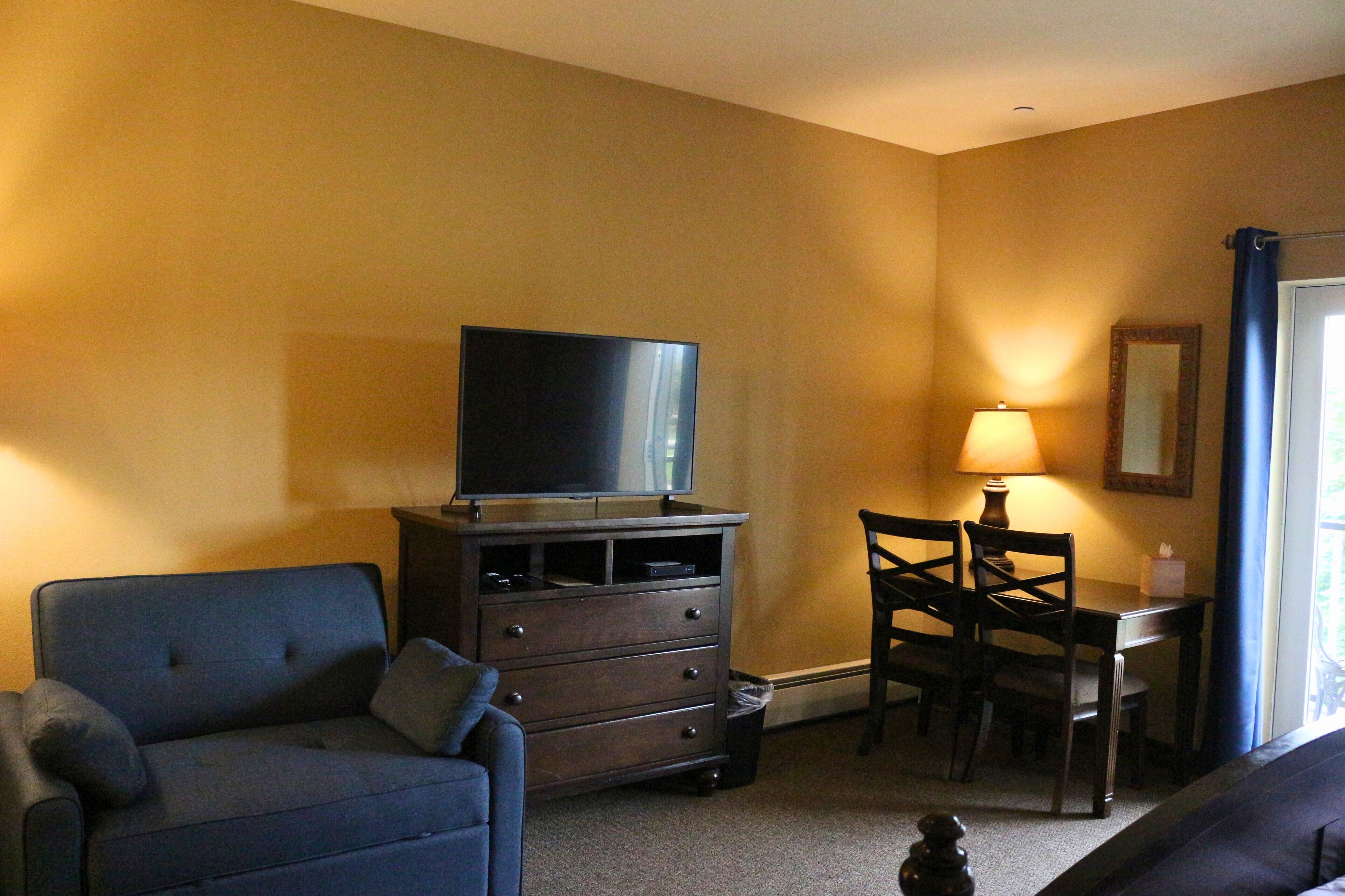 A living room with a sofa, a TV on a cabinet, a dining table with chairs, and a lamp.