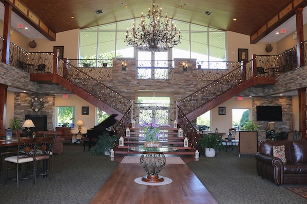 A spacious lobby with a grand staircase, a piano, and a chandelier.