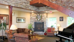 A cozy living room with a fireplace, a grand piano, and comfortable seating. - The Lodge at Woodstone Country Club (Danielsville)