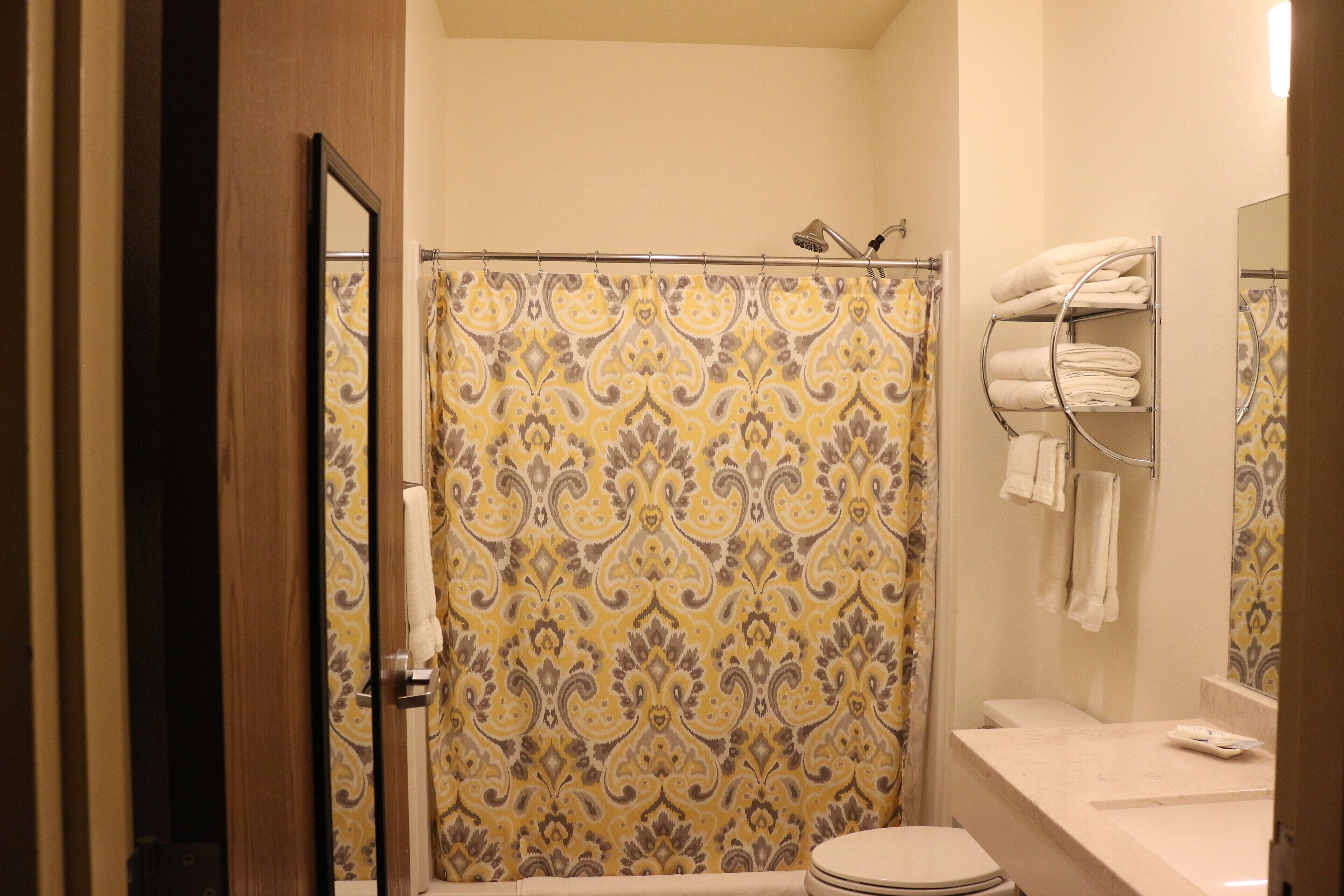 A bathroom with a shower curtain, a toilet, a sink with a mirror, and a towel rack with towels.
