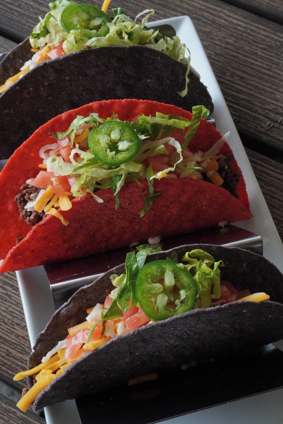 Three tacos with toppings on a white plate.