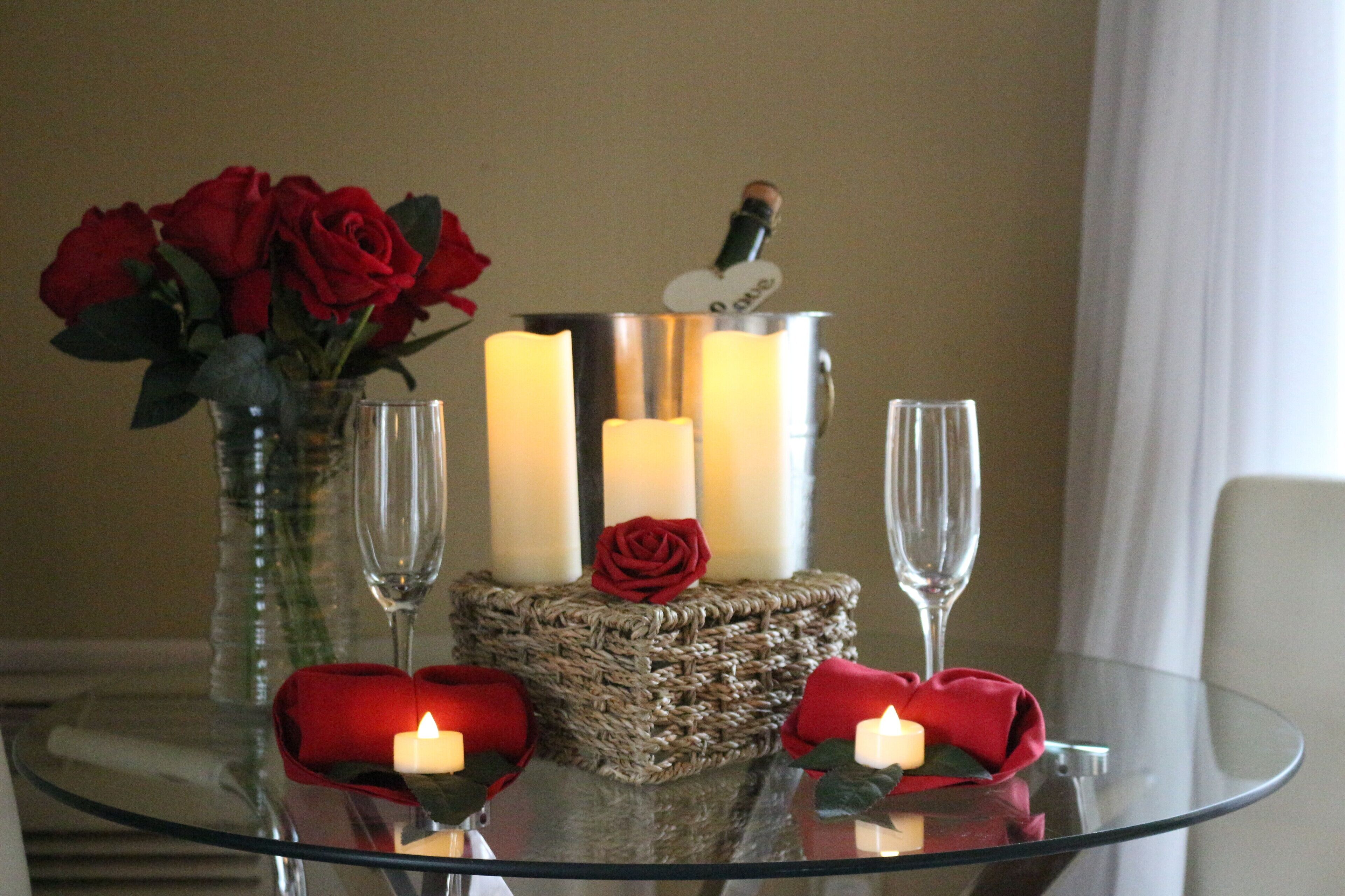 A table with candles, a vase of red roses, and a bottle of champagne.