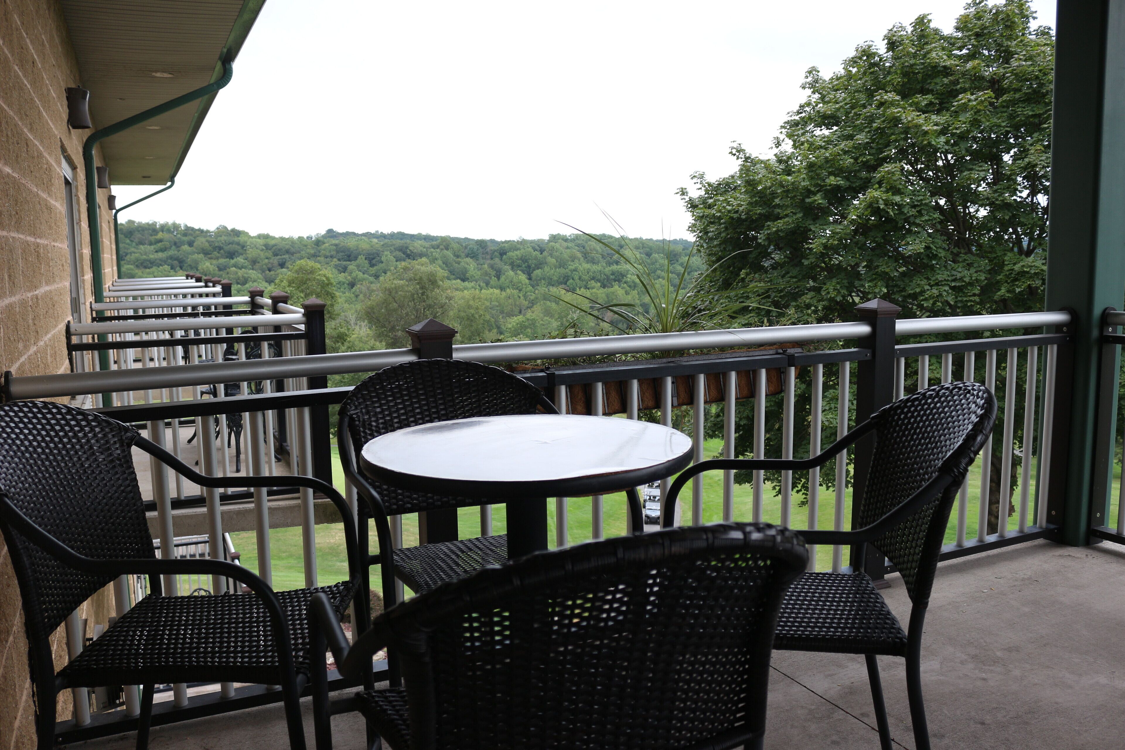 A balcony with wicker chairs and a table, overlooking a green landscape.