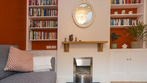 A cozy living room with a grey sofa, a fireplace, and bookshelves filled with books. - Colourful, homely 2 bed terrace - Pass the Keys (Shrewsbury)