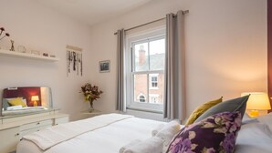 A neatly arranged hotel room with a bed, bedside table, lamp, and a window with curtains. - Colourful, homely 2 bed terrace - Pass the Keys (Shrewsbury)