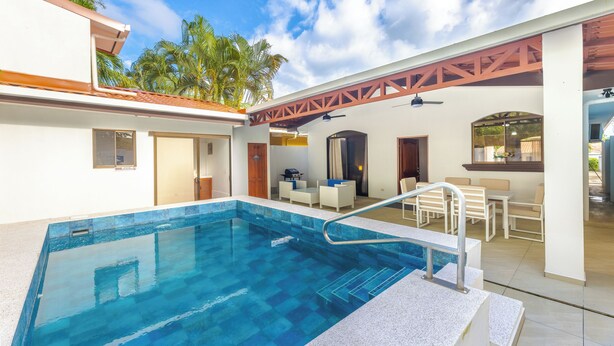 A swimming pool with a clear blue water, surrounded by a covered patio area with outdoor seating.