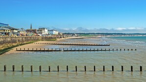 Une plage côtière bordée d’épis en bois, avec une promenade et des bâtiments en arrière-plan.