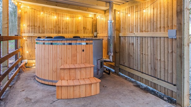 Un sauna en bois, doté d’un banc et d’un bain à remous, entouré de murs en bois et agrémenté d’une terrasse en bois.