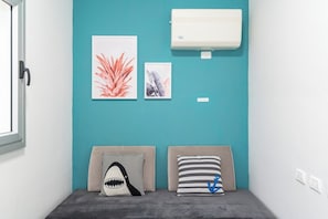 A room with teal walls, a white air conditioning unit, two headboards with pillows, and two framed artworks.
