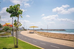 A paved pathway curving along a beach with a rocky outcrop in the distance. - Chic Coastal Escape Near the Beach by SeaNRent (Nahariya)