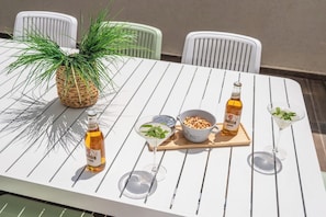 A white table with a bottle, a bowl of nuts, a martini glass, and a potted plant.