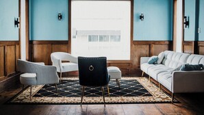 Ein Zimmer mit einem großen Fenster, einem gemusterten Teppich, einem weißen Sofa, einem schwarzen Sessel und einem weißen Ohrensessel.