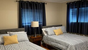 Ein Hotelzimmer mit zwei Betten, einem Nachttisch, einer Lampe und einem Fenster mit Vorhängen.