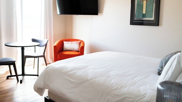Ein Hotelzimmer mit Bett, Wandfernseher, kleinem Tisch mit Stühlen und einem gerahmten Kunstwerk.