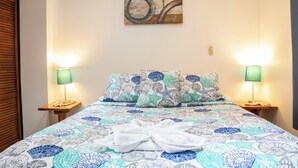 Una cama bien hecha con una colcha estampada, dos lámparas de noche y una obra de arte en la pared sobre la cama.