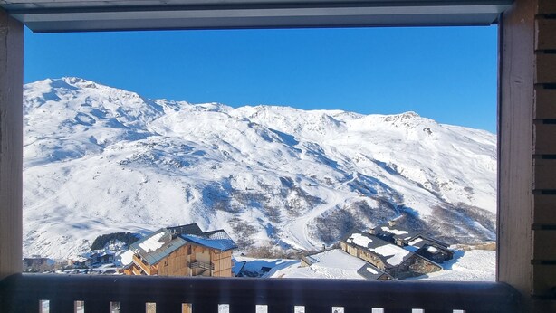 Une vue sur la montagne depuis un balcon doté de balustrades en bois, avec des sommets enneigés et un bâtiment au toit en pente.
