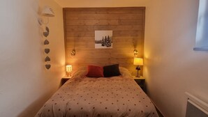 Une petite chambre à coucher accueillante, avec une tête de lit en bois, un lit recouvert d’une couverture à pois, deux lampes de chevet et un tableau accroché au mur.